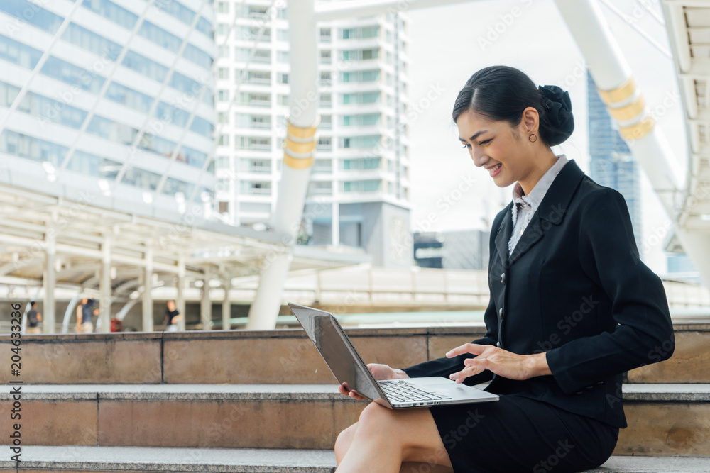 business woman smile and sit on the staircase and typing word into laptop, she happy because she talk with friend by video call business woman smile and sit on the staircase and typing word into laptop, she happy because she talk with friend by video call