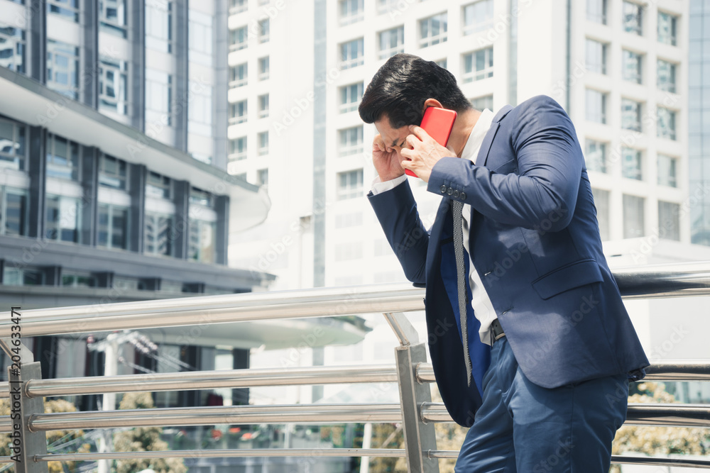 Serious worried businessman talking on red cell phone in the city. concept of Business failure and Sales decreased. Serious worried businessman talking on red cell phone in the city. concept of Business failure and Sales decreased.