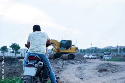 Engineer and Foreman on motocycle looking excavator on a construction site against urban scene