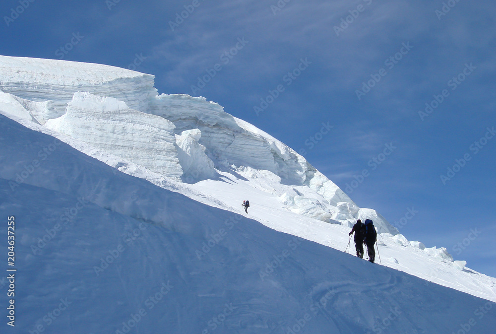 backcountry skiers hiking up a steep glacier and into the sunlight on their way to a high alpine peak near Zermatt