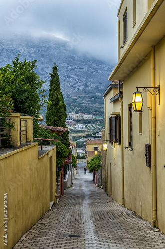 Fototapeta Naklejka Na Ścianę i Meble -  Archanes Town, Crete - Greece. Narrow paved alley with old traditional houses in Archanes on a rainy day. It is connected to Heraklion city with a 16 km long road. Storm, cloudy sky