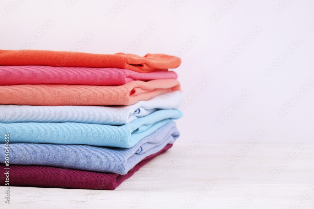 Stack of colorful perfectly folded t-shirts on white wooden texture table  background. Pile of different pastel color cotton shirts and sweaters.  Background, close up, front view, copy space for text. Stock Photo