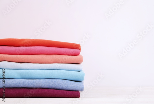 Stack of colorful perfectly folded t-shirts on white wooden texture table background. Pile of different pastel color cotton shirts and sweaters. Background, close up, front view, copy space for text.