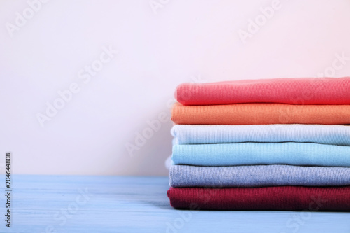 Stack of colorful perfectly folded t-shirts on white wooden texture table background. Pile of different pastel color cotton shirts and sweaters. Background, close up, front view, copy space for text.