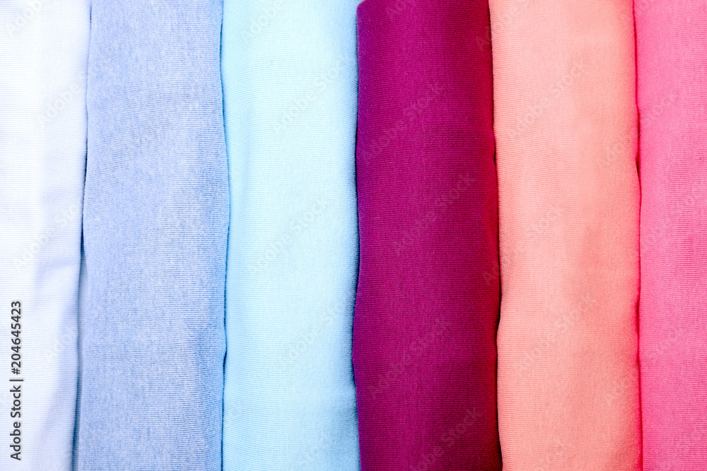 Close up of colorful clothes neatly rolled for saving luggage space, stack of cotton t-shirt rolls of different pastel colors on wooden texture table. Background, close up, copy space, top view.