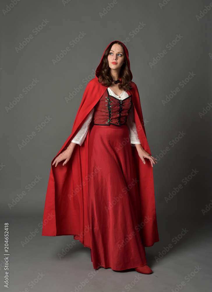 full length portrait of woman wearing red fantasy costume with cloak, standing pose on grey studio background. full length portrait of woman wearing red fantasy costume with cloak, standing pose on grey studio background.