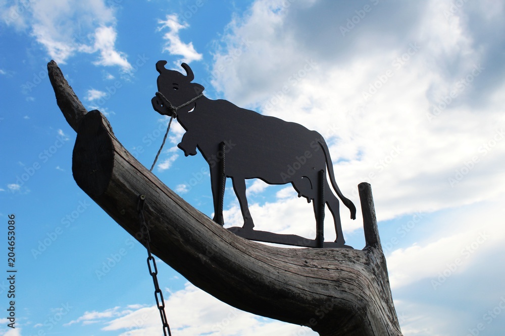 Kuh aus Metall auf Baumstamm vor blauem Himmel, Allgäu, Bayern foto de  Stock