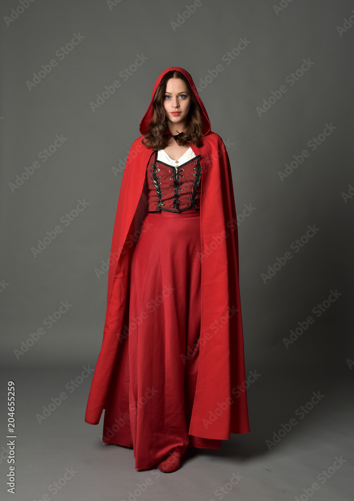 full length portrait of woman wearing red fantasy costume with cloak, standing pose on grey studio background.