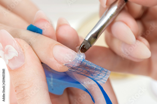 Nail Care And Manicure. Closeup Of Beautiful Female Hands Applying Transparent Nail Polish On Healthy Natural Woman s Nails In Beauty Salon. Manicurist Hand Painting Client s Nails.