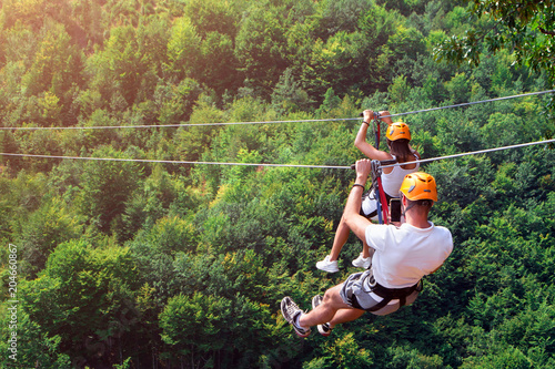Zipline is an exciting adventure activity. Man and woman hanging on a rope-way. Tourists ride on the Zipline through the canyon of the Tara River Montenegro. Couple in helmets is riding on a cable car photo