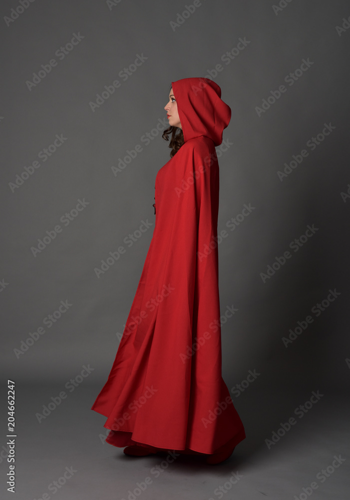 full length portrait of woman wearing red fantasy costume with cloak, standing pose on grey studio background. full length portrait of woman wearing red fantasy costume with cloak, standing pose on grey studio background.