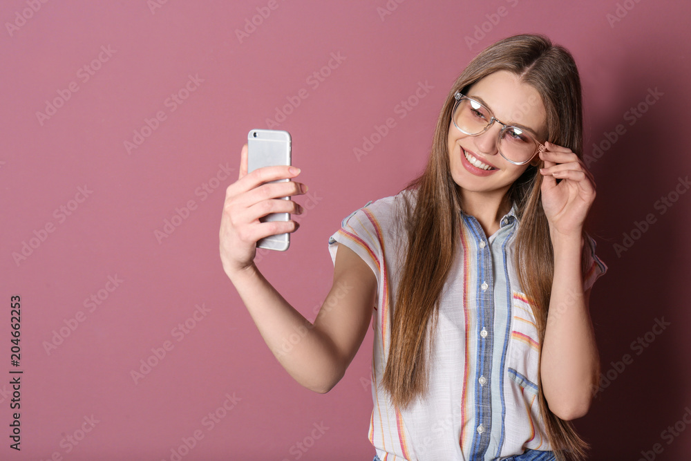Young beautiful woman taking selfie against color background