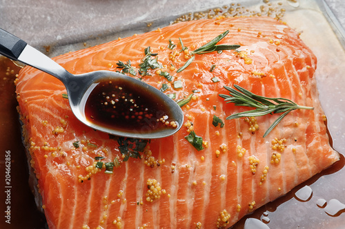 Spoon with marinade on raw salmon fillet, closeup photo