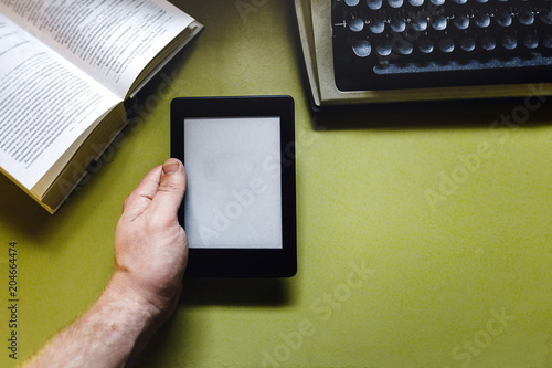 Man Holds E-Book In His Hand Against A Background Of A Paper Book And Typewriter, Top view