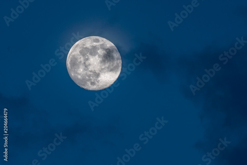 gorgeous full moon in a dark blue night sky gets covered by soft wispy dark clouds