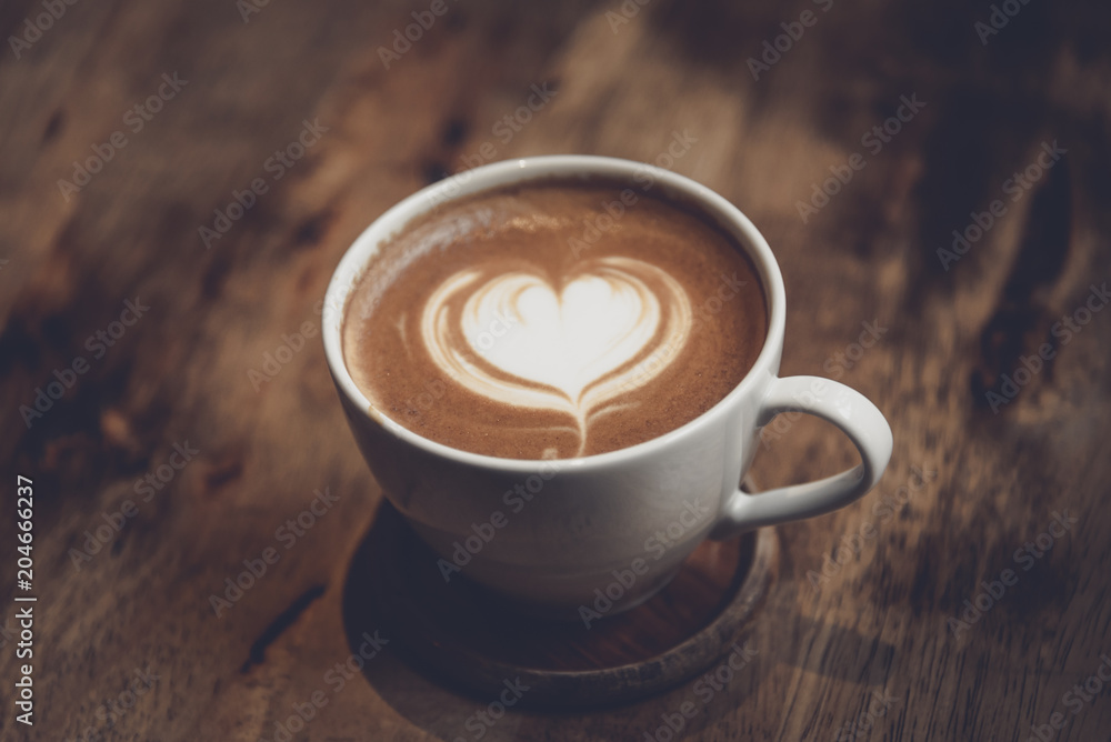 White cup of coffee with heart shape and aromatic smell on the table brown wood. White cup of coffee with heart shape and aromatic smell on the table brown wood.