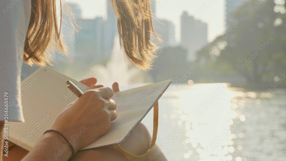 Young woman sitting on the bench in park and writing in diary, close-up - obrazy, fototapety, plakaty 