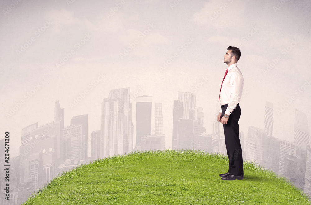 A confident male well looking office manager standing in small green grass in front of city landscape with tall buildings concept. A confident male well looking office manager standing in small green grass in front of city landscape with tall buildings concept.