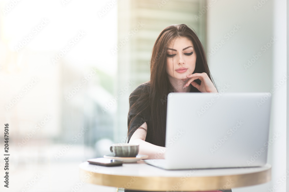 beautiful caucasian girl sitting at table in cafe with window on city street with cup of coffee working online on laptop beautiful caucasian girl sitting at table in cafe with window on city street with cup of coffee working online on laptop