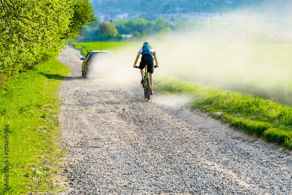 Fototapeta premium A cyclist riding a dusty road behind a car in a dusty cloud. Cycling on holiday in the Czech Republic. 