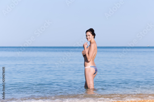 Young woman in swimming trunks standing knee-deep in water