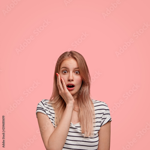 Photo of amazed surprised young Caucasian female model stares at camera, sees something unbelievable, being stunned, isolatd over pink studio background. People, emotions and feelings concept
