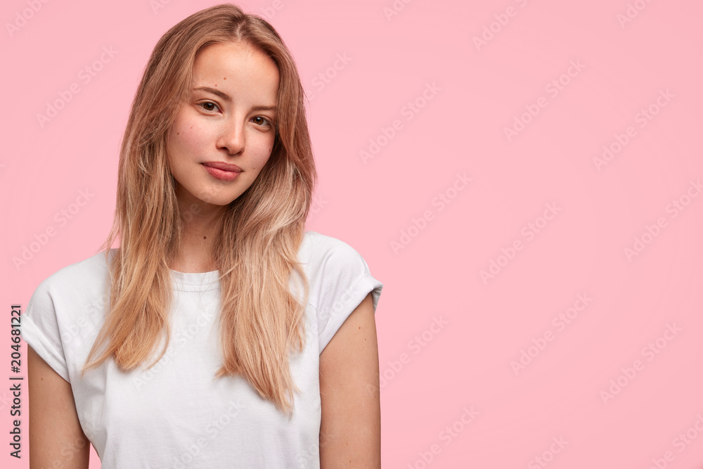 Horizontal portrait of attractive female with pleasant appearance, wears white casual t shirt, poses against pink background with copy space. Gorgeous satisfied woman student rejoies success Horizontal portrait of attractive female with pleasant appearance, wears white casual t shirt, poses against pink background with copy space. Gorgeous satisfied woman student rejoies success