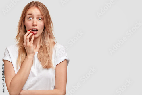 Studio shot of amazed Caucasian female looks with wide opened mouth and eyes popped out, feels puzzled as remembers necessary important information, isolated over white background, copy space