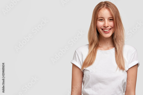 Photo of happy young female freelancer with pleasant smile on face, wears whi...