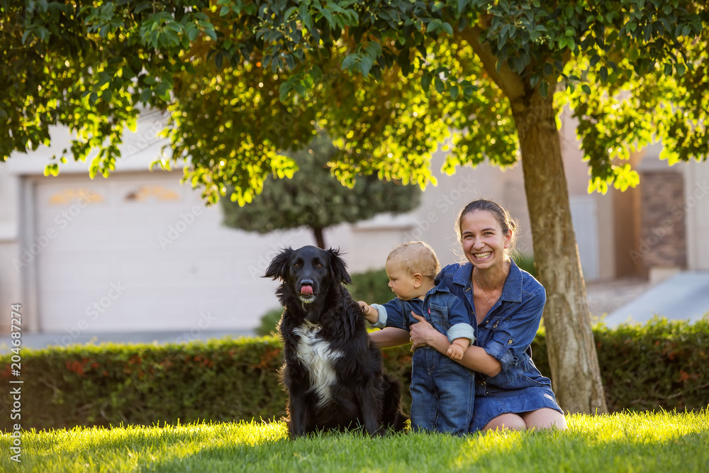 A mother with baby son and black dog in green neighborhood A mother with baby son and black dog in green neighborhood