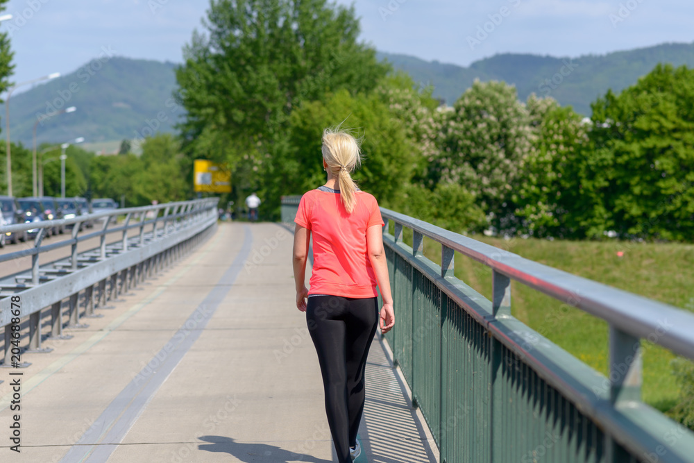Blond woman jogging across a pedestrian bridge
