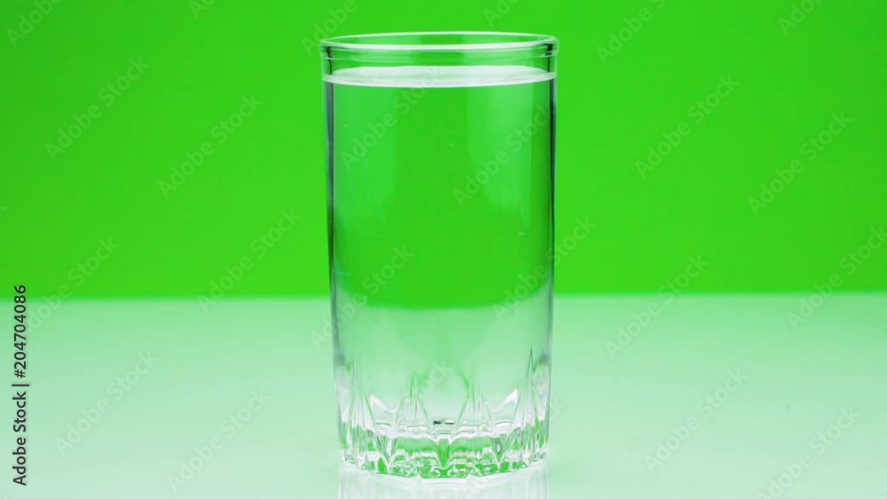 Close-up shot of An effervescent tablet against pain falls into a glass and dissolves slow-motion shot of aspirin on a green background Close-up shot of An effervescent tablet against pain falls into a glass and dissolves slow-motion shot of aspirin on a green background