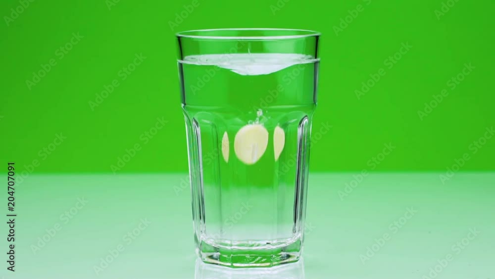 An effervescent tablet against pain falls into a glass and dissolves Close-up slow-motion shot of aspirin on a green background An effervescent tablet against pain falls into a glass and dissolves Close-up slow-motion shot of aspirin on a green background