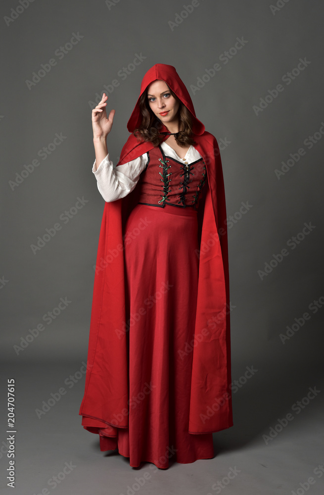 full length portrait of woman wearing red fantasy costume with cloak, standing pose on grey studio background. full length portrait of woman wearing red fantasy costume with cloak, standing pose on grey studio background.