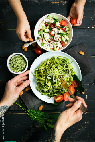 Woman hands holds zucchini raw vegan pasta with avocado dip suace, spinach leaves and cherry tomatoes on plate. On dark background. Vegetarian healthy food