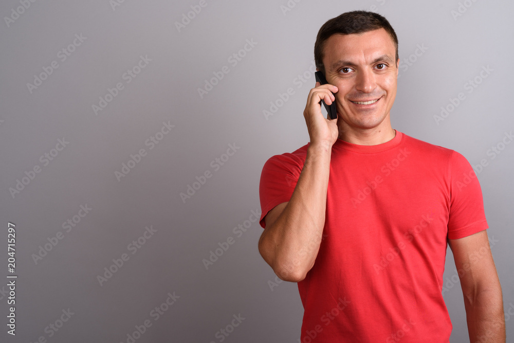 Man wearing red shirt while using mobile phone against gray back Man wearing red shirt while using mobile phone against gray back