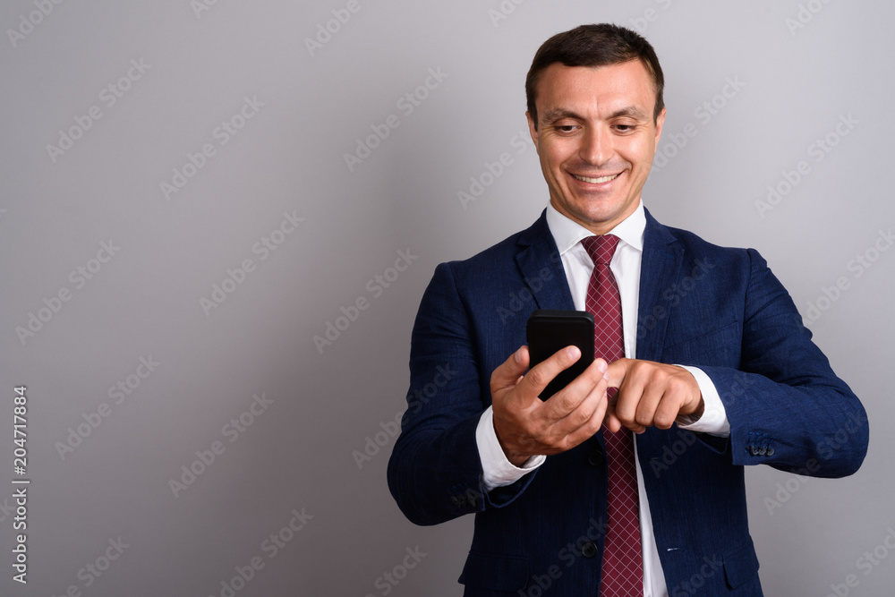 Businessman wearing suit while using mobile phone against gray b Businessman wearing suit while using mobile phone against gray b