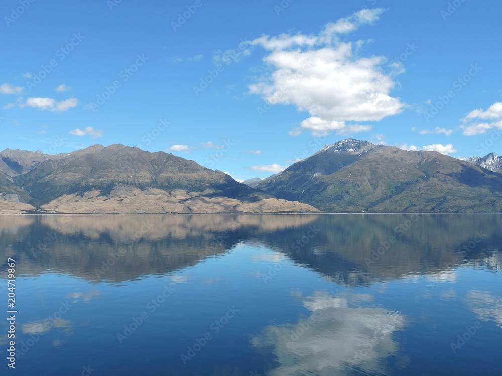 Glassy lake reflecting mountains and blue sky, Lake Wanaka, New Zealand Glassy lake reflecting mountains and blue sky, Lake Wanaka, New Zealand
