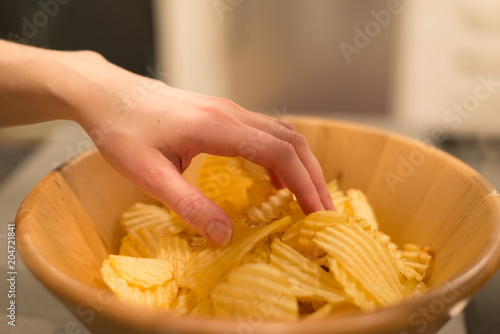 Hand Reaching Potato Chips in Wooden Bowl