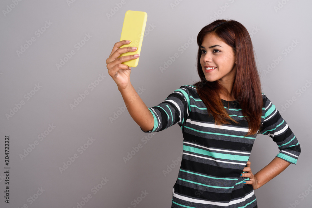 Young beautiful Indian woman using mobile phone against gray bac Young beautiful Indian woman using mobile phone against gray bac