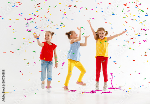 happy children on holidays jumping in multicolored confetti on white