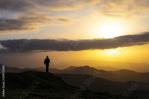 Man celebrating success on top of a mountain in sunrise.
