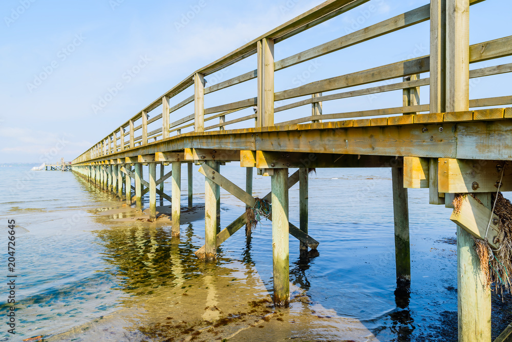 Borstahusen, Sweden - The underside of a wooden pier with logs driven into the sea bottom. Shallow water on a calm and windless day. Borstahusen, Sweden - The underside of a wooden pier with logs driven into the sea bottom. Shallow water on a calm and windless day.