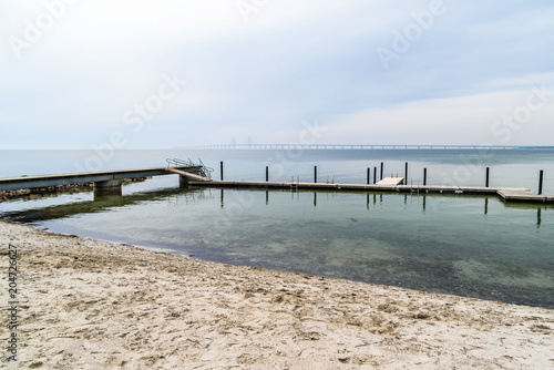 Kalgshamn  Sweden - A bathing pier on a sandy shore on a calm and foggy day. The Oresund bridge is visible in the distant mist.
