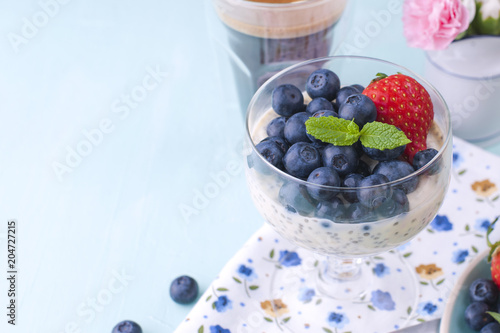 A glass of coffee and pudding chia with blueberries and strawberries for breakfast. Vegetarian food. Blue background. Napkin with flowers. Bright colors