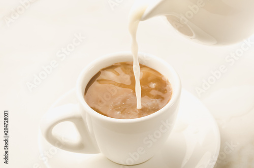 Fotografía milk is added to coffee cup/milk is added to coffee cup on a white background