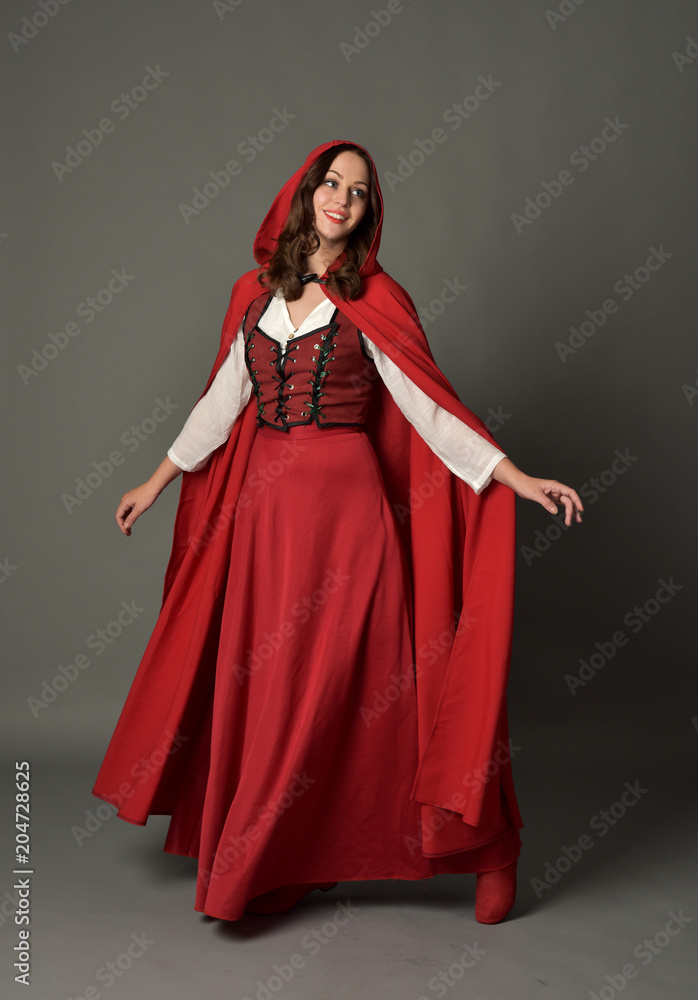 full length portrait of woman wearing red fantasy costume with cloak, standing pose on grey studio background.