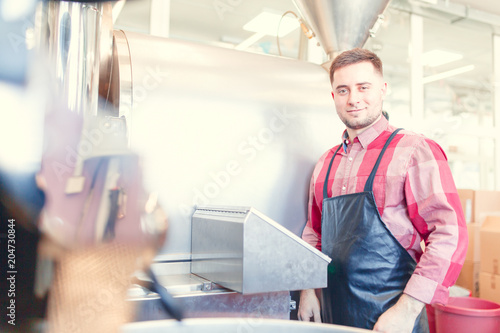 Photo of brunette businessman in apron standing next to industrial roster