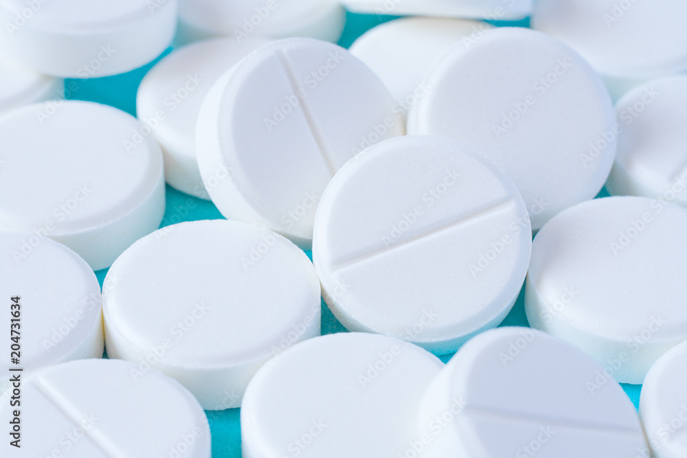 Close up view of a heap of white round pills on a turquoise table as background (macro)