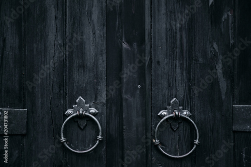 Old black wooden door with ring doorknobs. Close up view, texture, pattern